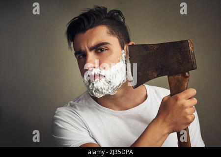 Es ist das richtige Werkzeug für den Job. Aufnahme eines hübschen jungen Mannes, der sich mit einem Holzfäller den Bart rasiert. Stockfoto