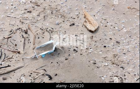 Ein Zeichen der covid Zeiten, liegt eine chirurgische Maske auf einem Strand abgelegt. Stockfoto