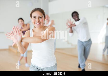 Fröhliche junge hispanische Frau, die mit der Gruppe energischen Tanz praktiziert Stockfoto