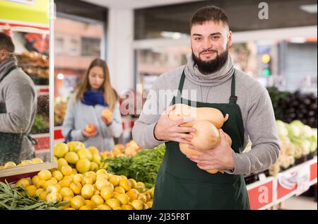 Porträt eines positiven Mannes in Schürze, der kleine dekorative Kürbisse verkauft Stockfoto