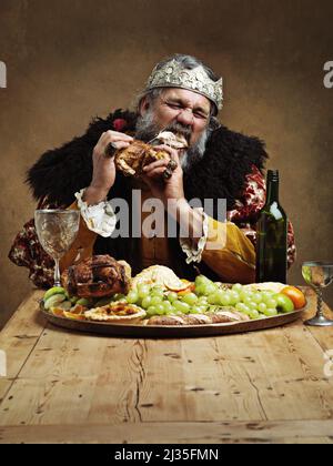 Das Regieren ist ein hungriger Geschäftsbetrieb. Ein reifer König, der allein in einem Bankettsaal schmallt. Stockfoto