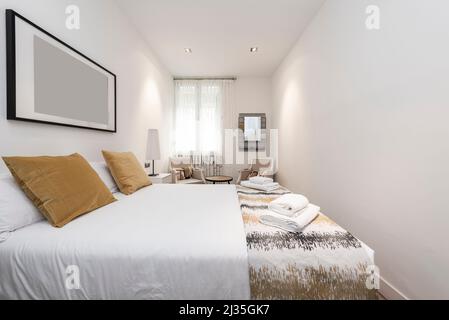 Schlafzimmer mit einem großen Doppelbett mit goldenen Kissen, Sesseln und Handtüchern auf dem Bett in einer Ferienwohnung Stockfoto