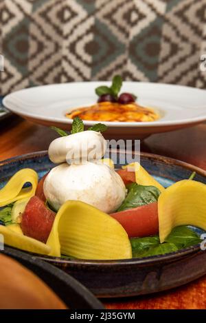 Großartiges italienisches Rezept für Burrata-Käse mit Tomaten, Basilikum, Salat und gekochten Nudelblättern Stockfoto