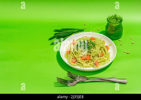 Pasta mit Lachs, wildem Lauch-Pesto und Parmesan. Frische Spaghetti und Grüns. Gesundes veganes Essen, trendiges hartes Licht, dunkler Schatten. Leuchtend grüne Hintergrundrou Stockfoto