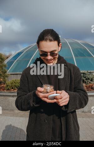 Junge schwule Hipster essen Erdnüsse auf der Straße lächelnd glückliche Sonnenbrille Stockfoto