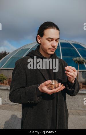 Junge schwule Hipster essen Erdnüsse auf der Straße lächelnd glückliche Sonnenbrille Stockfoto