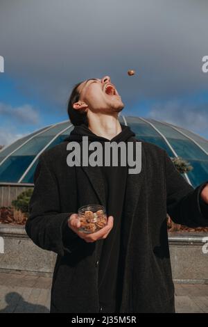 Junge schwule Hipster essen Erdnüsse auf der Straße lächelnd glückliche Sonnenbrille Stockfoto
