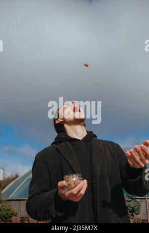 Junge schwule Hipster essen Erdnüsse auf der Straße lächelnd glückliche Sonnenbrille Stockfoto