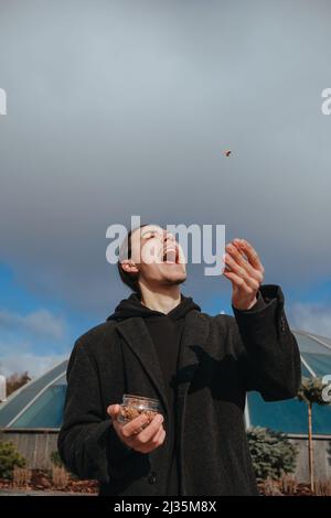 Junge schwule Hipster essen Erdnüsse auf der Straße lächelnd glückliche Sonnenbrille Stockfoto