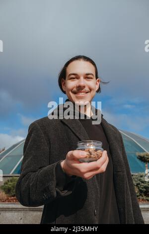 Junge schwule Hipster essen Erdnüsse auf der Straße lächelnd glückliche Sonnenbrille Stockfoto