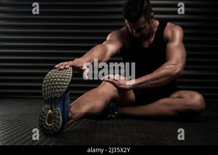 Sicherstellen, dass sein Körper bereit für das Training ist. Studio-Aufnahme eines sportlichen jungen Mannes, der sich vor dem Training aufwärmt. Stockfoto