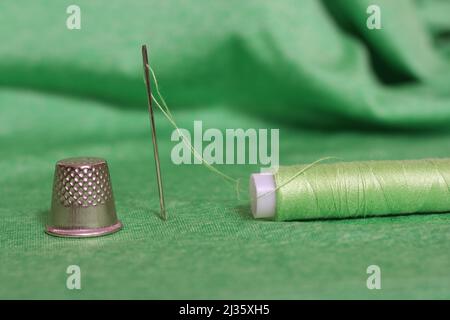 Spule aus grünem Faden, Nimble und Nadel auf grünem Stoff in Nahaufnahme Stockfoto