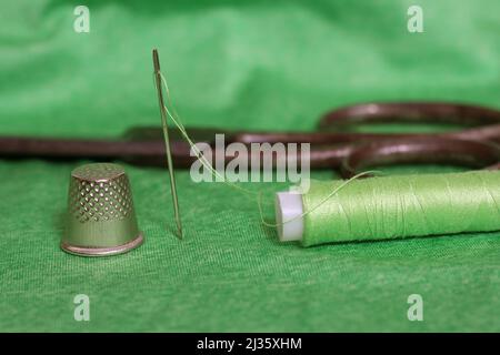 Spule aus grünem Faden, Nimble und Nadel auf grünem Stoff in Nahaufnahme Stockfoto