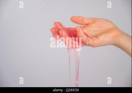 Roter Schleim, der aus der Hand einer Frau auf einem weißen Hintergrund herabfließt. Stockfoto