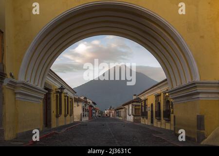 Sonnenaufgang auf Antigua Guatemala empfängt der Vulkan Agua, der durch den Santa Catalina Arch gesehen wird, die ersten Sonnenstrahlen Stockfoto