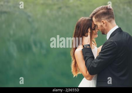 Nahaufnahme eines Brautpaares, das vor der Kulisse eines Bergsees posiert. Naturlandschaft. Eleganter Hochzeitshintergrund. Elegant Stockfoto