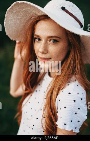 Nahaufnahme eines rothaarigen Mädchens mit Sommersprossen und langen Haaren, das Hut trägt und im Freien posiert. Beauty Mode Modell. Schönheit Haut weibliches Gesicht Stockfoto