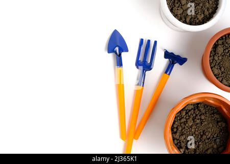 Blumentöpfe mit Erde und dekorativen Gartenwerkzeugen auf weißem Hintergrund Stockfoto