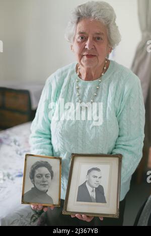 Sie werden immer in Erinnerung bleiben. Porträt einer älteren Frau mit alten Schwarz-Weiß-Fotos eines Mannes und einer Frau. Stockfoto