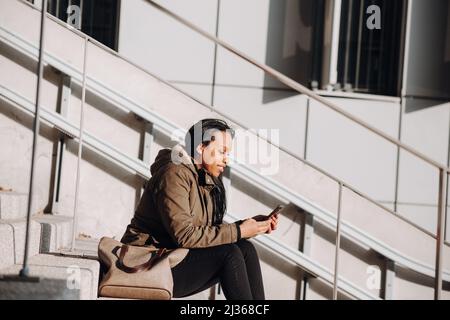 Eine junge, multirassische Dame, die mit ihrem Smartphone in der Sonne sitzt Stockfoto