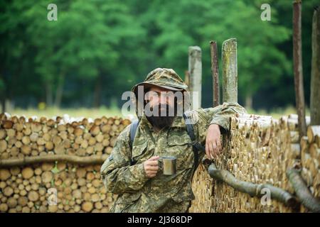 Porträt des Reisenden Mann trinken Tee oder heißen Kaffee mit Emaille-Tasse, Metall-Becher. Reise Lifestyle Landschaft und Abenteuer Konzept. Mensch in der Natur. Stockfoto