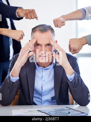 Ich fühle mich von allen Seiten angegriffen. Porträt eines reifen Geschäftsmannes, der gestresst in einer anspruchsvollen Büroumgebung aussieht. Stockfoto