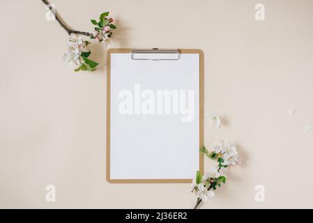 Clipboard Tablet Pad mit leerem Kopierraum und weißen Apfelblüten auf beigem Hintergrund. Flach liegend, Vorlage für Draufsicht. Weiblicher Schreibtisch Stockfoto