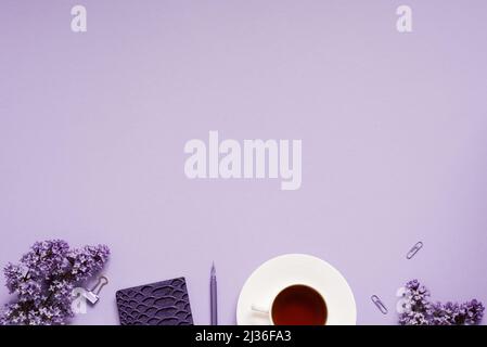 Der Arbeitsplatz eines Bloggers oder Freiberuflers Flat lag mit einer Tasse Kaffee, Notizbüchern und fliederfarbenen Zweigen, Papeterie auf fliederem Hintergrund mit einem Copy Spa Stockfoto