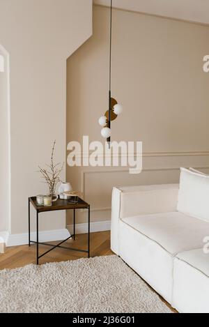 Ein Sofa aus hellem Stoff und ein Couchtisch aus Holz mit Dekor in einem gemütlichen skandinavischen minimalistischen Wohnzimmer in der Wohnung Stockfoto