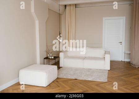 Ein Wohnzimmer mit einem weißen Stoffsofa und einem Couchtisch. Minimalistisches skandinavisches Interieur mit Lampe und Teppich Stockfoto