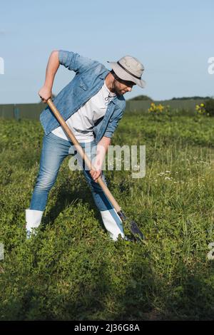 In voller Länge Ansicht von Landwirt in Krempe Hut und Denim Kleidung graben im Feld Stockfoto