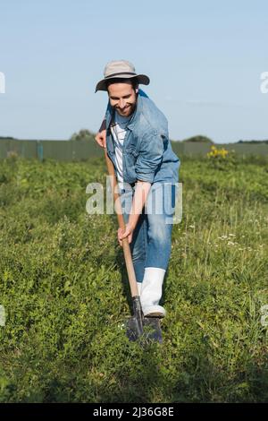 In voller Länge Ansicht von zufrieden Landwirt in Krempe Hut und Denim Kleidung graben im Feld Stockfoto