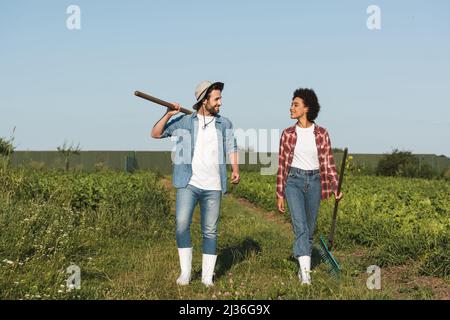 In voller Länge sehen Sie junge, interracial Bauern lächeln einander an, während sie auf dem Feld spazieren Stockfoto