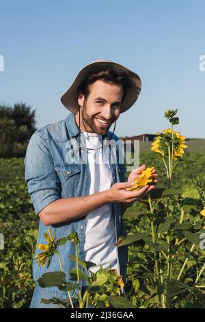Glücklicher Bauer lächelt der Kamera zu und zeigt Sonnenblumen auf dem Feld Stockfoto