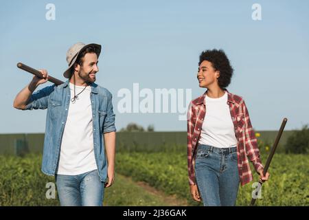 Junge interrassische Bauern lächeln sich gegenseitig auf dem grünen Feld an Stockfoto