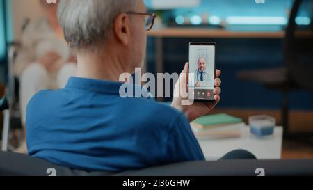 Ältere Personen, die einen Arzt auf einer Videokonferenz anrufen, um an einer Konsultation teilzunehmen, und Mobiltelefon für Telemedizin und Telemedizin verwenden. Pensionierter Erwachsener im Gespräch mit einem Spezialisten für Online-Videoanruf. Stockfoto