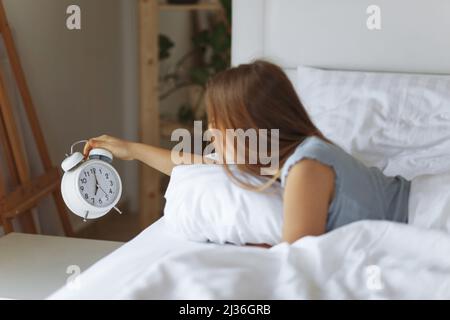 Frau schlafen auf dem Bett schaltet den Wecker am Morgen aufwachen, Selective Focus. Junge Frau greift, um Wecker auszuschalten, am frühen Morgen Stockfoto