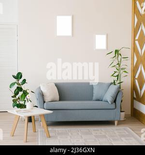 Das Interieur eines modernen Wohnzimmers in hellen Farben. Sofa mit Kissen, Couchtisch, Ficus und Bambus in einer Kanne, geschnitzte Holzwand mit geometrischem p Stockfoto