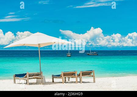 Liegestühle aus Holz an einem Sandstrand vor dem Meer mit Booten, Sansibar Tansania Stockfoto