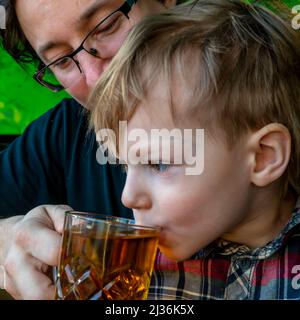 Konzept für das Glück der Familie am Morgen. Vater und Sohn trinken Tee in der Küche, gemalt wie ein Wald. Vater und Sohn haben Spaß. Stockfoto