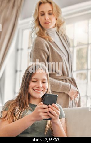 Manchmal ist Platz notwendig. Aufnahme einer reifen Mutter, die heimlich nachsieht, was ihre Töchter zu Hause am Telefon machen. Stockfoto