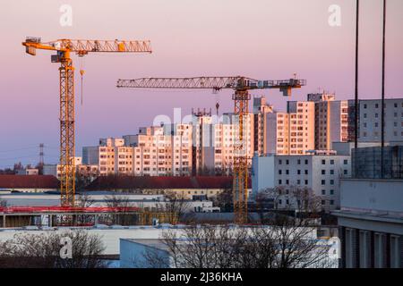 Berlin, Deutschland. 27. März 2022. Baukräne leuchten im Licht der aufgehenden Sonne vor einer Wohnanlage golden. Quelle: Fernando Gutierrez-Juarez/dpa-Zentralbild/dpa/Alamy Live News Stockfoto