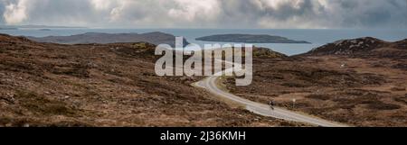 Ein einsamer Radfahrer auf dem Brae der Achnahaird, mit dem Summer Isles im Hintergrund, an der Westküste von Schottland. Stockfoto