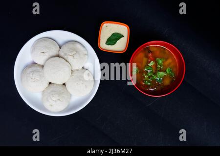 Untätig in weißer Schale, Sambar in roter Schale mit Kokosnuss Chutney in Schale, isoliert auf schwarzem Hintergrund, untätig in weißer Platte, Sambar in roter runder Schale, Coc Stockfoto