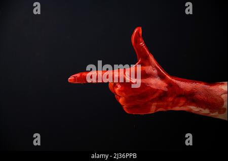 Die blutige Hand einer Frau zeigt eine Geste einer Waffe auf schwarzem Hintergrund. Stockfoto