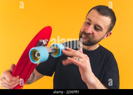 Junge zufrieden sympathisch bärtigen europäischen Mann hält ein Skateboard orange Hintergrund Studio Schuss Medium shot . Hochwertige Fotos Stockfoto