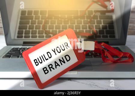 Erstellen Sie Ihren Markentext, der auf einem roten Namensschild auf einem Laptop oder Notebook angebracht ist. Stockfoto