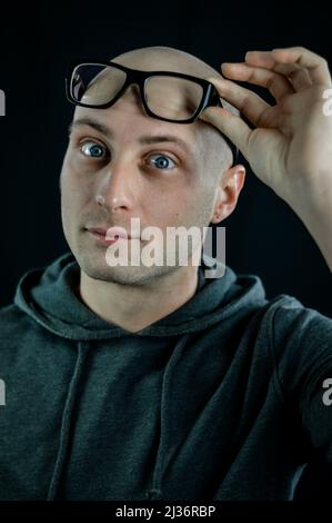 Porträt eines kahlen jungen Mannes, der schwarze Brillen auf seiner Stirn hält, während er ernst aussieht Stockfoto