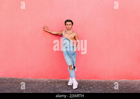 Stilvoller Typ, der eine pinke Wand anlehnt und die Kamera anschaut. Junger, hübscher Mann, der im Freien steht. Stockfoto