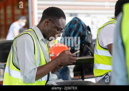 Afrikanischer schwarzer Arbeiter entspannen beim Spielen Handy bei der Mittagspause Ruhe glückliches Lächeln. Stockfoto